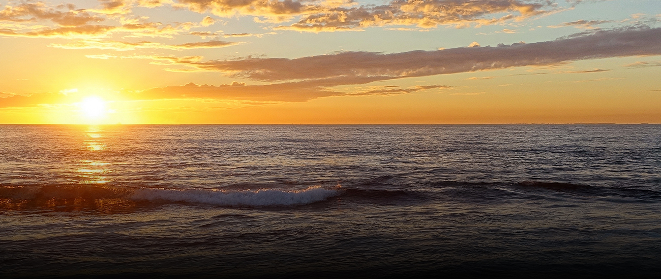 A wave during sunset, with vibrant colors illuminating the sky and reflecting on the water.